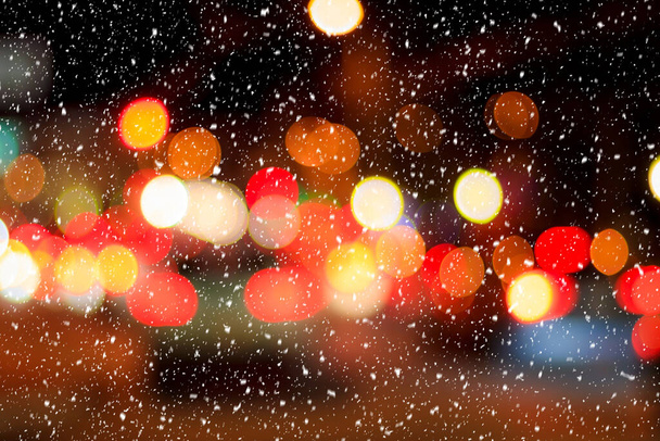 Falling snow against the background of blurry lights of headlights of cars and the night city. Winter snowfall concept. Abstract bright bokeh. - Photo, Image