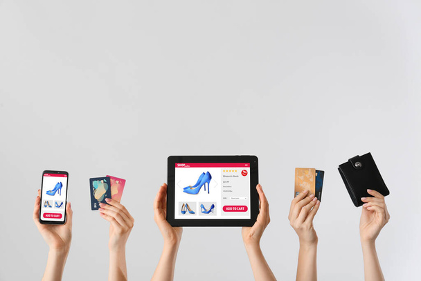 Vrouwelijke handen houden moderne apparaten met open pagina van online schoenenwinkel op het scherm, portemonnee en creditcards op lichte achtergrond - Foto, afbeelding