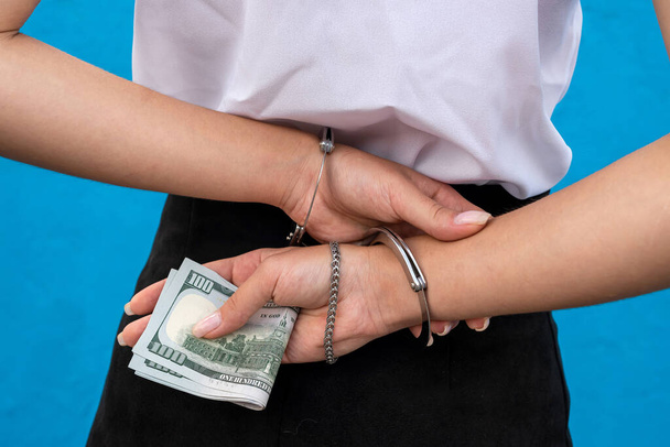 female hands in handcuffs hold dollars isolated on blue.  Prisoner or arrested - Photo, Image