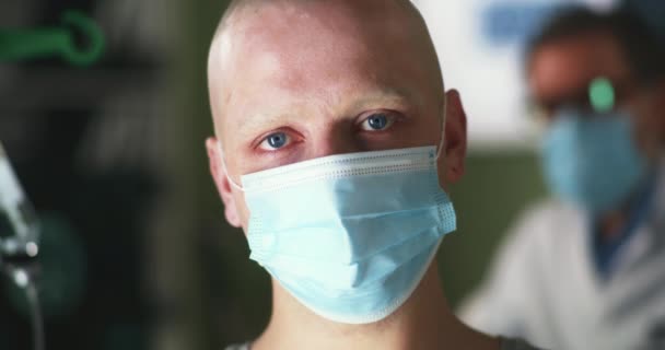 Лысый мужчина в маске смотрит на камеру в больнице - Кадры, видео