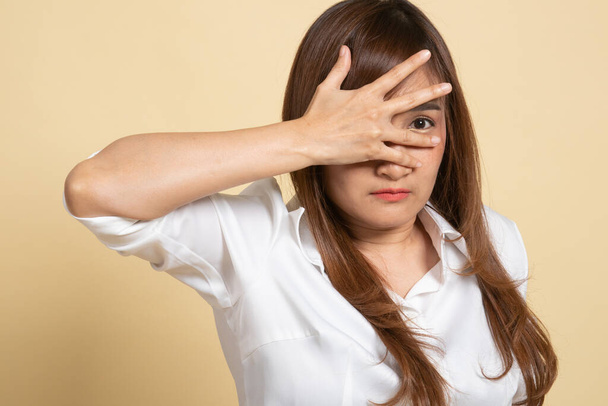 Beautiful young Asian woman peeking through fingers on beige background - Fotografie, Obrázek