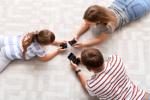 Family with mobile phones lying on floor at home - Foto, Bild