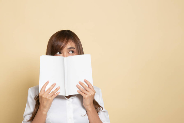 Young Asian woman with a book cover her face on beige background - Fotoğraf, Görsel