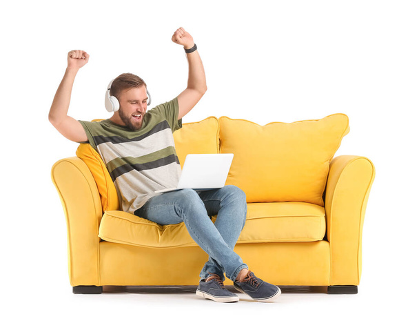 Happy man with headphones and laptop on sofa against white background - Foto, Imagen