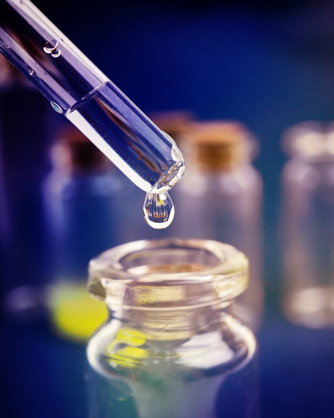 gota de líquido de una pipeta en una botella médica, concepto de investigación, nuevos medicamentos y ciencia, sobre un fondo rosa brillante, azul y púrpura - Foto, Imagen