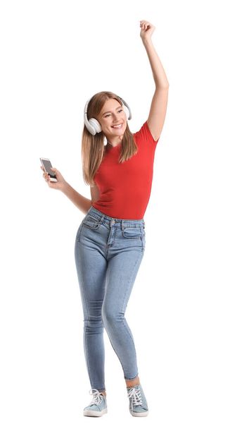 Young woman with mobile phone and headphones dancing on white background - Фото, изображение