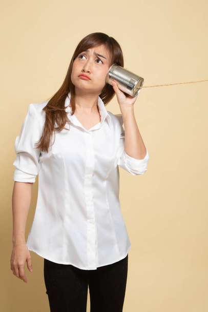 Young Asian woman with tin can phone on beige background - Φωτογραφία, εικόνα