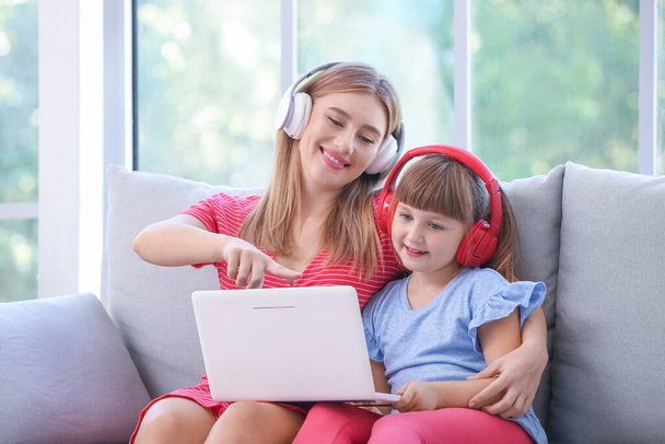 Mother and daughter with headphones and laptop at home - 写真・画像