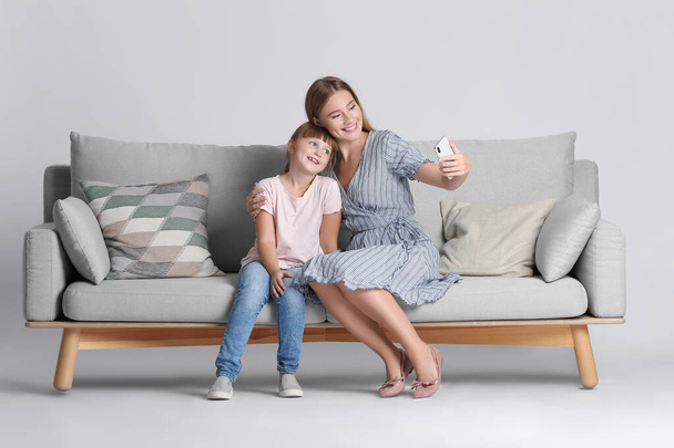 Madre e figlia scattare selfie sul divano sullo sfondo leggero - Foto, immagini