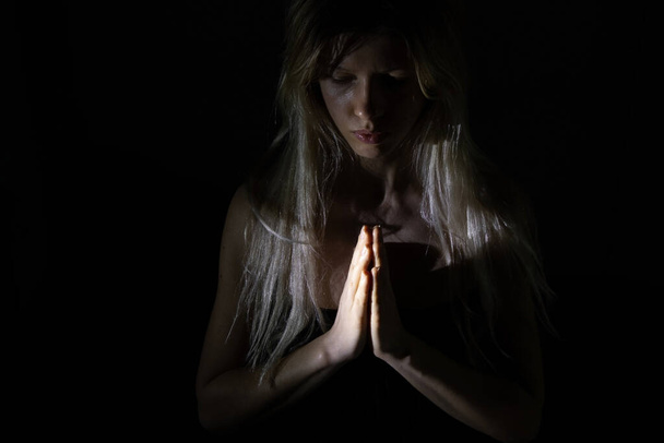 Karanlıktaki kız zayıf bir ışıkla Tanrı 'ya dua ediyor, en iyisini umuyor. - Fotoğraf, Görsel