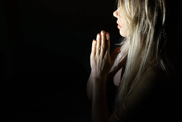 Karanlıktaki kız zayıf bir ışıkla Tanrı 'ya dua ediyor, en iyisini umuyor. - Fotoğraf, Görsel