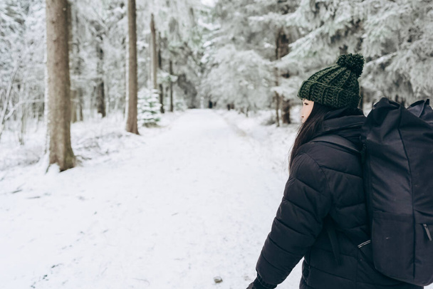暖かい冬の服と美しい雪に覆われた森林の背景に大きなバックパックを持つアクティブな若い観光客。ハイキング。女性の観光。 - 写真・画像
