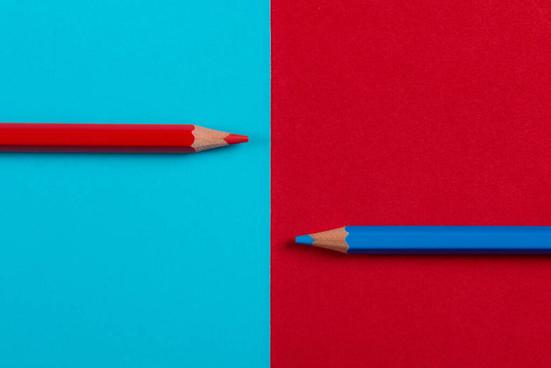 Dos lápices de colores dividen una imagen por la mitad en dos colores diferentes, rojo y azul - Foto, Imagen