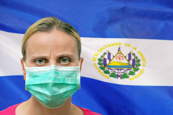 Жінка з маскою дивиться на камеру на фоні прапора Сальвадо. Концепція уваги до всесвітнього поширення коронавірусу по всьому світу. Коронавірус у Сальвадо - Фото, зображення