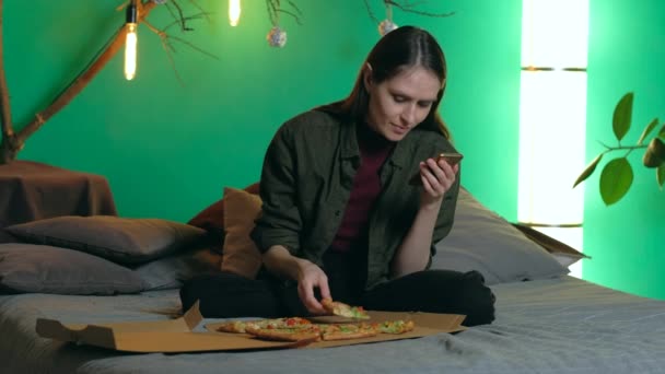 Evdeki kanepede oturan ve pizza yiyen bir kadın. akıllı telefon - Video, Çekim