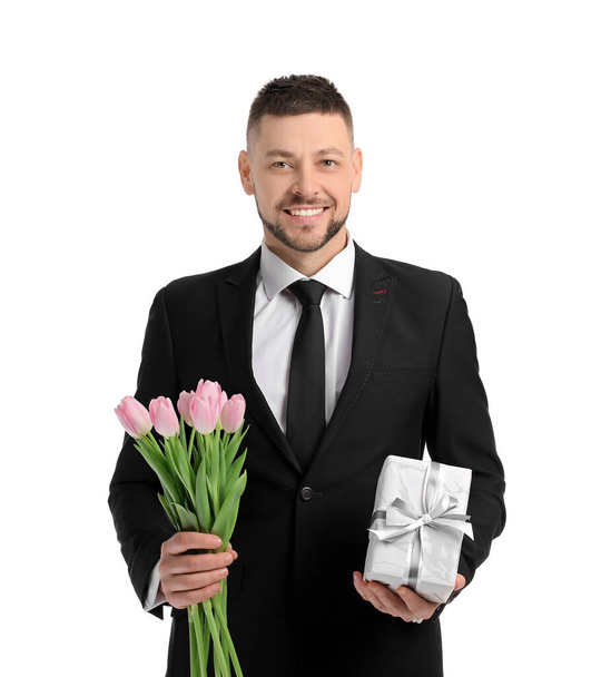 Knappe man met boeket van mooie bloemen en cadeau op witte achtergrond - Foto, afbeelding