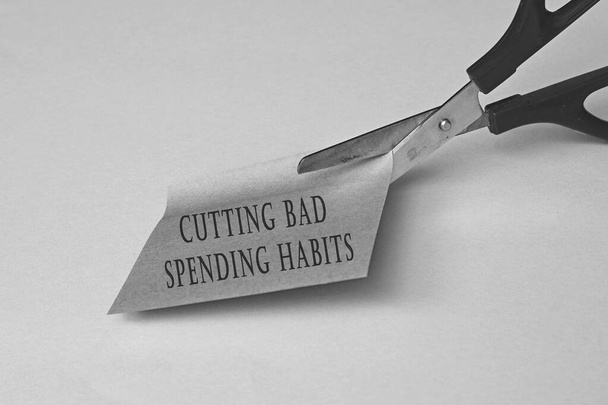 Scissors that cut yellow notepad with text on a black and white background. Spending habits concept - Photo, Image