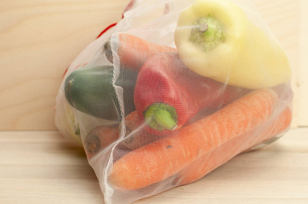 a white thin plastic net which is reusable for shopping of food filled with fresh vegetables - Valokuva, kuva