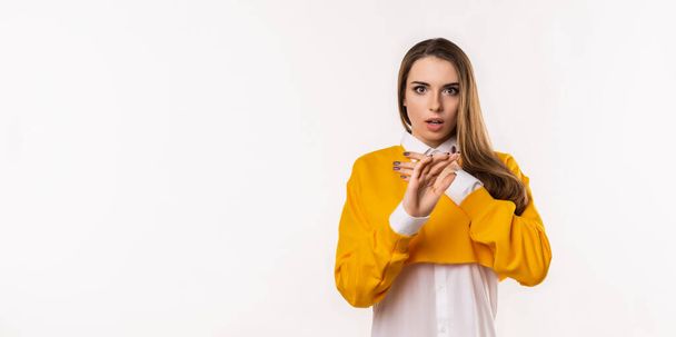 Portrait of startled young brunette woman raising hands and gasping worried, staring shocked and confused at camera. Studio shot, white background. Mock up copy space - Foto, Imagem