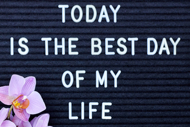 De inscriptie Vandaag is de beste dag van mijn leven op een zwarte achtergrond, een roze orchidee in de hoek. - Foto, afbeelding