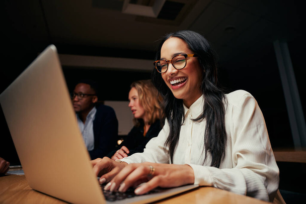Close-up of successful smiling young African American businesswoman sitting near coworkers using laptop in office - Fotó, kép