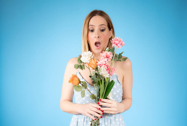 Portrait of a beautiful young woman holding big bouquet of flowers isolated over blue background. - Photo, Image