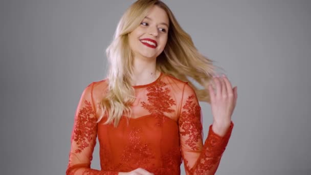 Χαμογελαστή γυναίκα με κόκκινο φόρεμα που αγγίζει τα μαλλιά στο στούντιο - Πλάνα, βίντεο