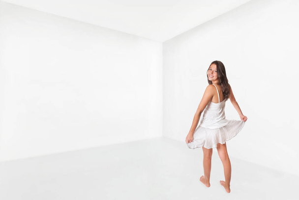Schattig meisje draagt rok en top en danst gelukkig in een lege witte kamer - Foto, afbeelding
