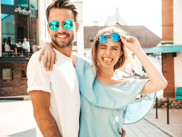 Portrait of smiling beautiful female and her handsome boyfriend. Woman in casual summer jeans dress. Happy cheerful family. Female having fun. Couple posing on the street background in sunglasses - Fotó, kép