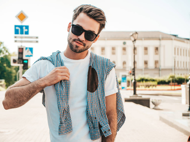 Portrait of handsome smiling stylish hipster lambersexual model.Man dressed in white T-shirt. Fashion male posing in the street in sunglasses  - Φωτογραφία, εικόνα