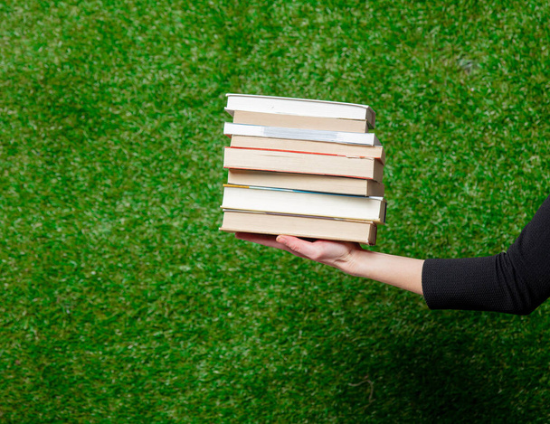 Vrouwelijke hand houden boeken over groen gras op de achtergrond - Foto, afbeelding