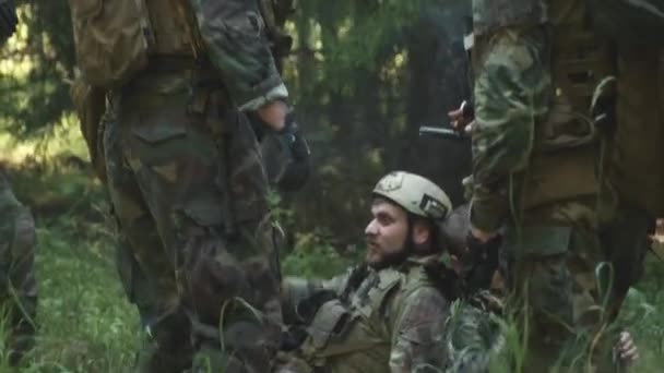 Tilting handheld footage of squad of cheerful young caucasian soldiers relaxing in forest before secret operation, talking while smoking cigarettes - Footage, Video