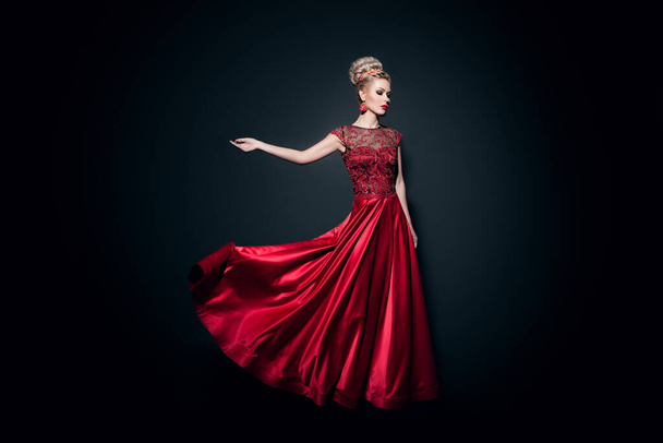 полный вид длиной большой молодой женщины одеваются в длинное пламя красное платье с поднятыми руками, на черном фоне. - Фото, изображение