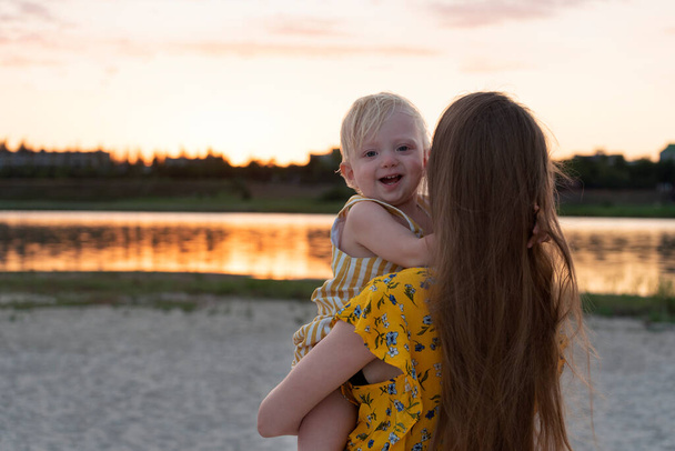 Matka trzyma uśmiechnięte dziecko przed rzeką w zachodzie słońca - Zdjęcie, obraz