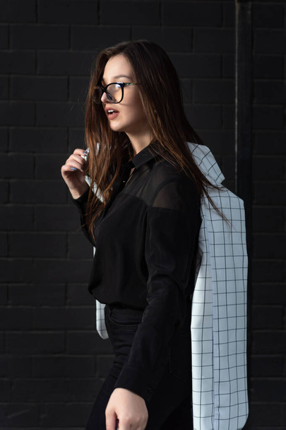 Retrato de mujer joven con estilo en gafas y ropa negra sobre fondo negro. Marco vertical. - Foto, Imagen