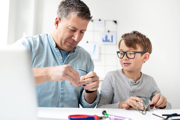 Father and son repairing an electrical outlet while sitting at a desk. Learn for life concept - Zdjęcie, obraz