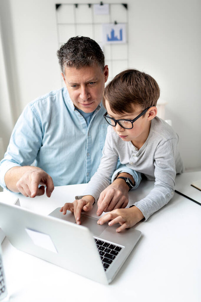 Apa és fia ül a laptop előtt, otthonról dolgoznak.. - Fotó, kép
