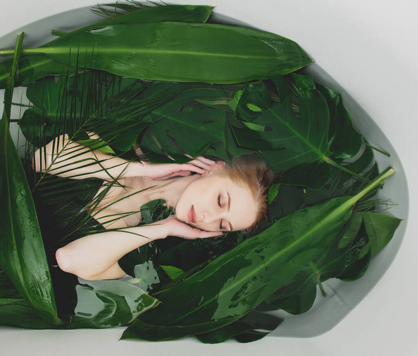 Beautiful white woman lying in bathtub with palm leaves around - Zdjęcie, obraz