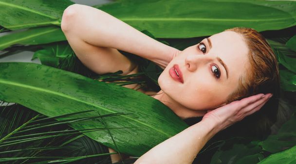 Hermosa mujer blanca acostada en la bañera con hojas de palma alrededor - Foto, imagen