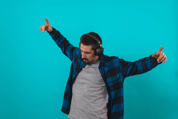Young handsome man dancing and singing songs listening to music in headphones on a blue background. Happy male enjoying music. - Fotografie, Obrázek