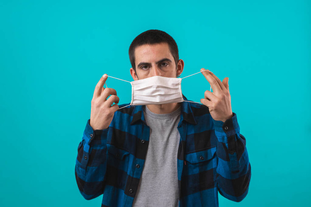 Portrait of handsome young man with surgical medical mask looking at camera. Indoor studio shot, isolated on blue background. - Valokuva, kuva