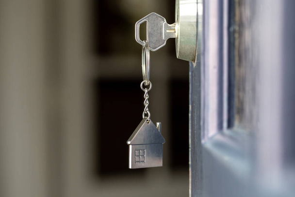 Open deur naar een nieuw huis met sleutel en huisvormige sleutelhanger. Hypotheek, investeringen, vastgoed, vastgoed en nieuw woonconcept - Foto, afbeelding