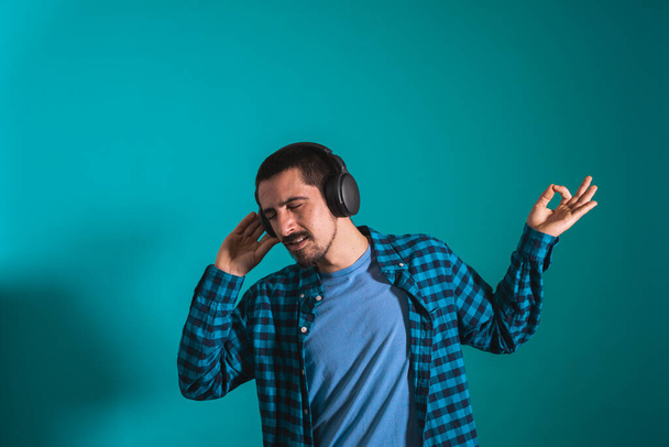 Young handsome man dancing and singing songs listening to music in headphones on a blue background. Happy male enjoying music. - Φωτογραφία, εικόνα
