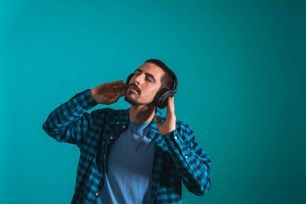 Young handsome man dancing and singing songs listening to music in headphones on a blue background. Happy male enjoying music. - Photo, Image