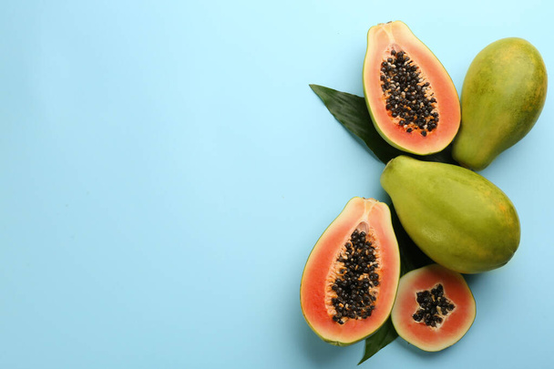 Fresh ripe papaya fruits with green leaves on light blue background, flat lay. Space for text - Photo, image