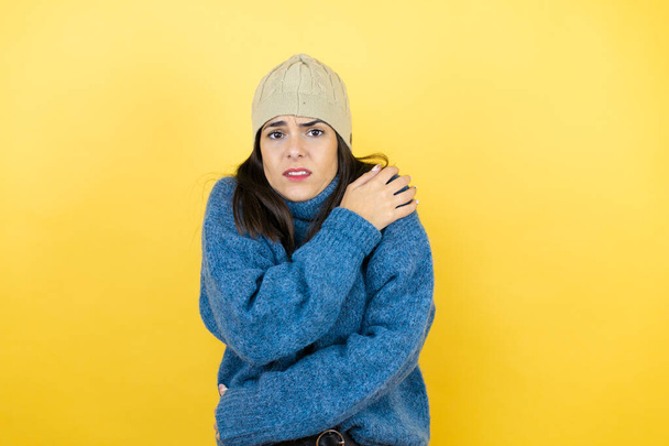 Mujer hermosa joven con suéter azul casual y sombrero de lana temblando y congelándose para el frío de invierno con expresión triste y de choque en la cara - Foto, Imagen