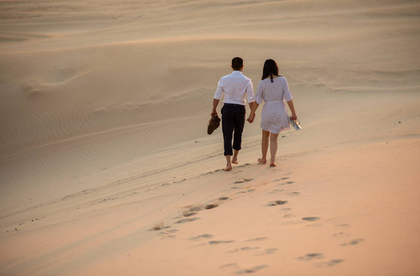 Ζευγάρι περπατά στην άμμο αμμόλοφο κρατώντας τα χέρια - Φωτογραφία, εικόνα
