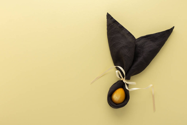 Conejito de Pascua abstracto de servilleta gris oscuro y huevo pintado de oro sobre fondo amarillo, concepto festivo de Pascua - Foto, imagen