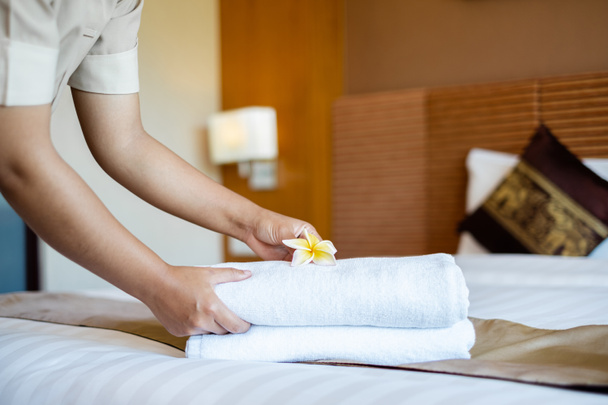 A hotel maid stacked towels on the bed and placed flowers on the towels in a hotel room. - Zdjęcie, obraz