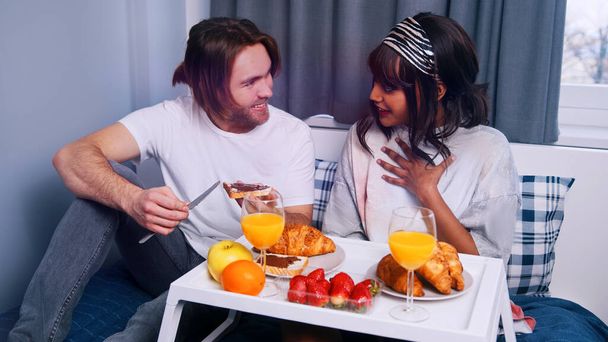 Young multiracial newlywed couple having breakfast in the bed on the honeymoon - Foto, Bild